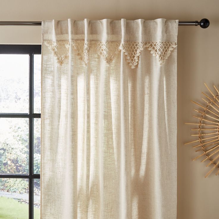 a window with white curtains and a sunburst hanging on the wall next to it