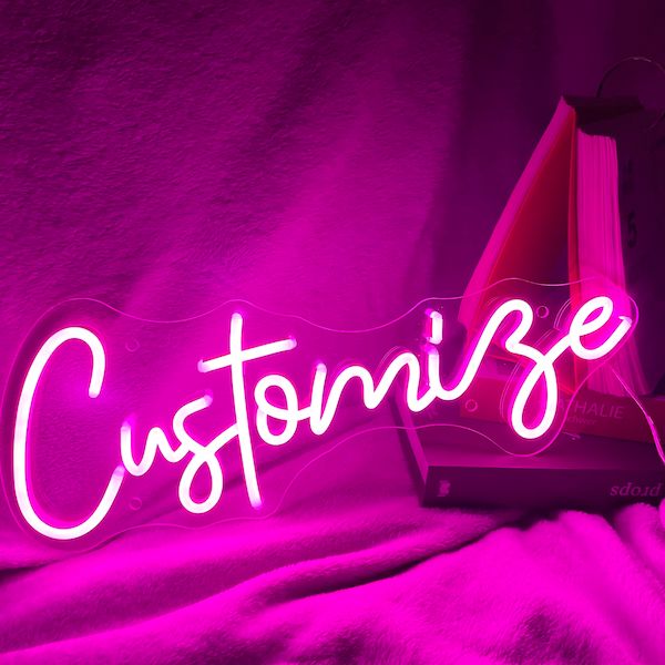 a pink neon sign that says customize on top of a bed covered in blankets