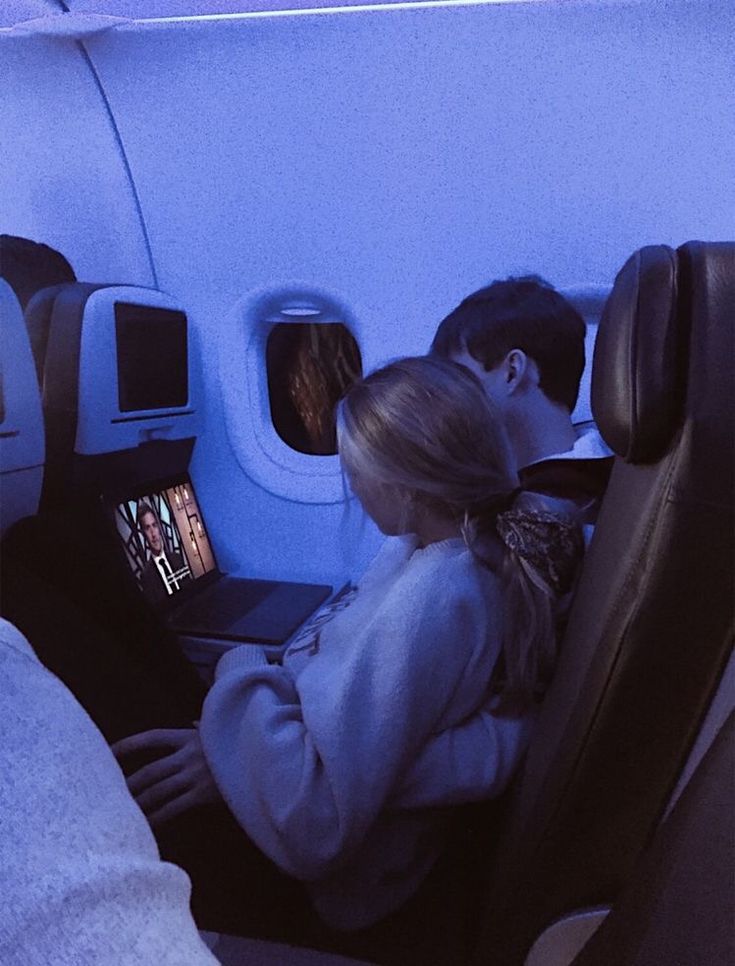 two people sitting in an airplane looking at their laptops