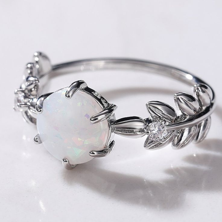 an opal and diamond ring on a white surface with the center stone surrounded by leaves