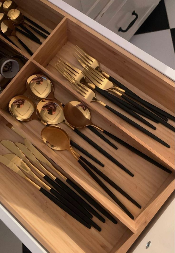 an open drawer with gold and black utensils