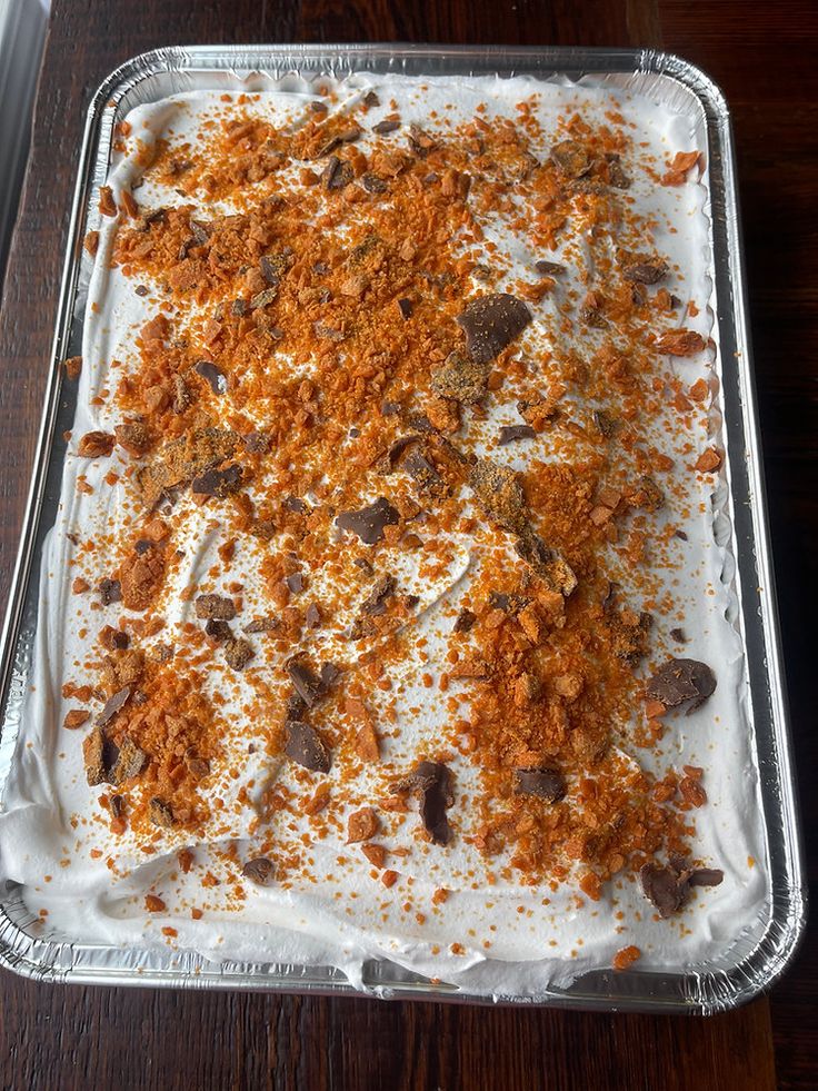 an uncooked dessert in a pan on a wooden table with white frosting and brown sprinkles