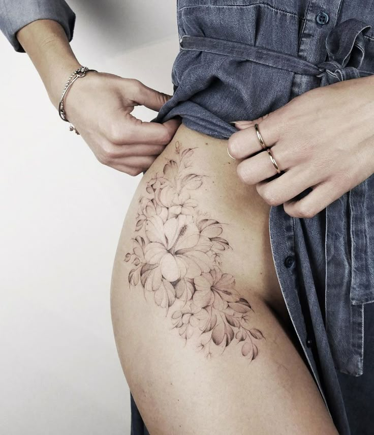 a woman is showing off her flower tattoo on her lower back side view while holding onto the thigh