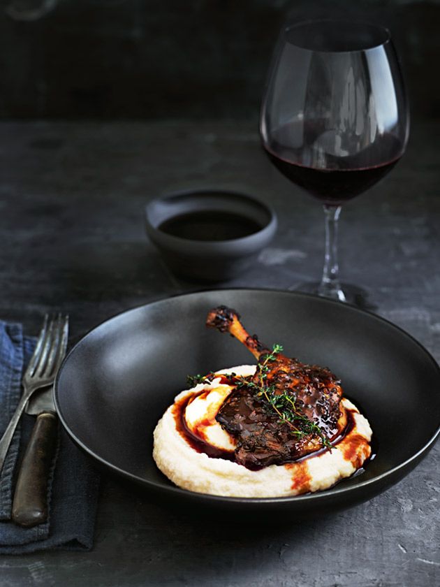 a black plate topped with meat and mashed potatoes next to a glass of wine