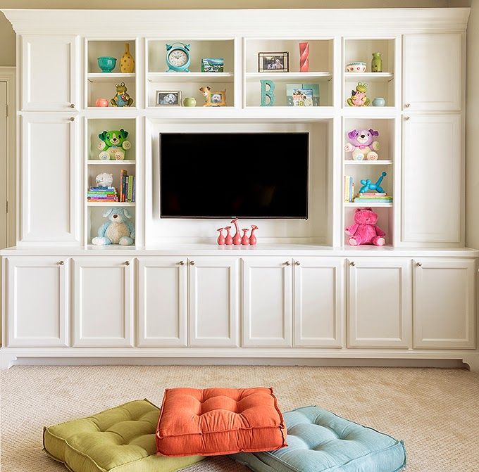 the entertainment center is decorated in white and has colorful pillows on the floor for seating