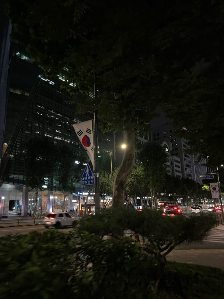 a city street at night with cars driving on the road and tall buildings in the background