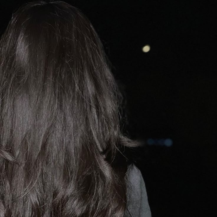 the back of a woman's head with long dark hair in front of a full moon