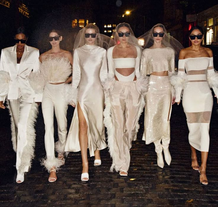 models in white outfits walk down the street at night with one woman wearing sunglasses on her head