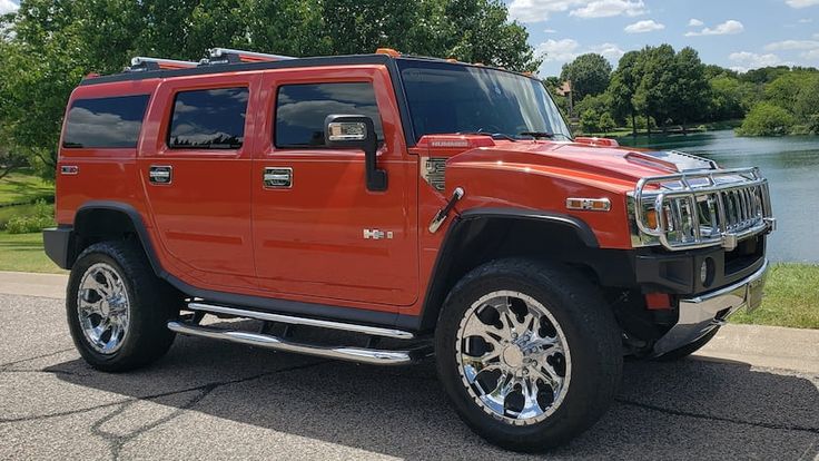 a red hummer truck is parked on the side of the road near some water