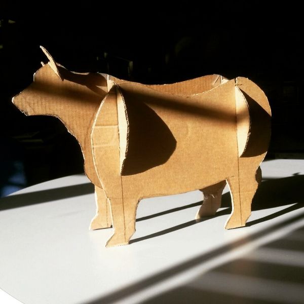 an origami cow standing on top of a white table with the sun shining through it