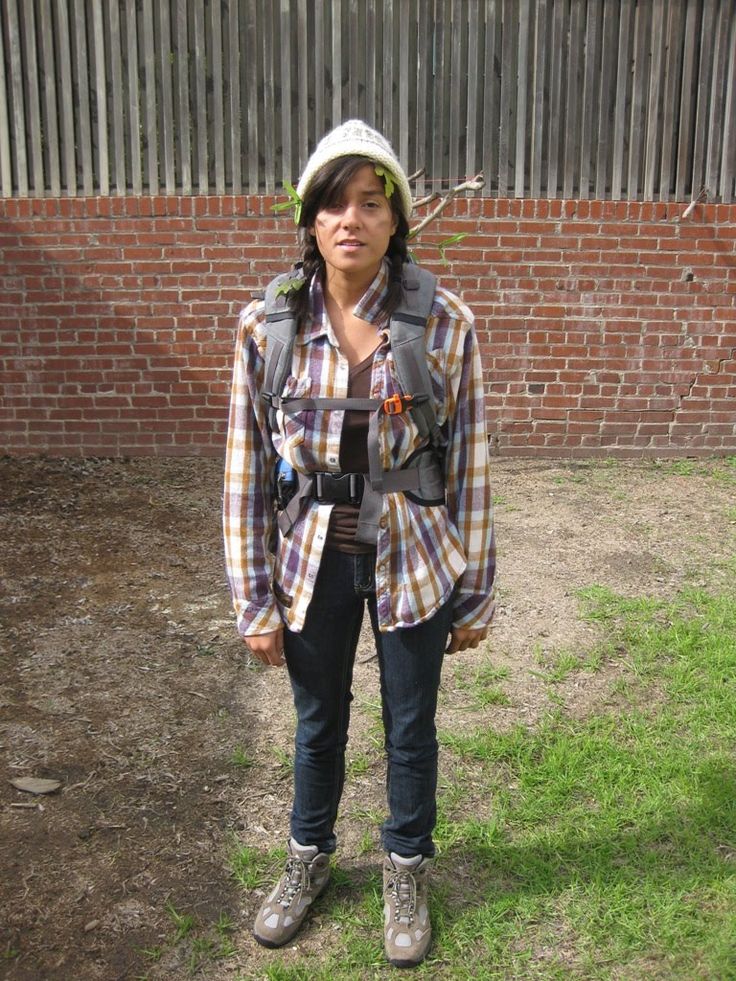 a woman standing in front of a brick wall wearing a plaid shirt and jeans with a hat on her head