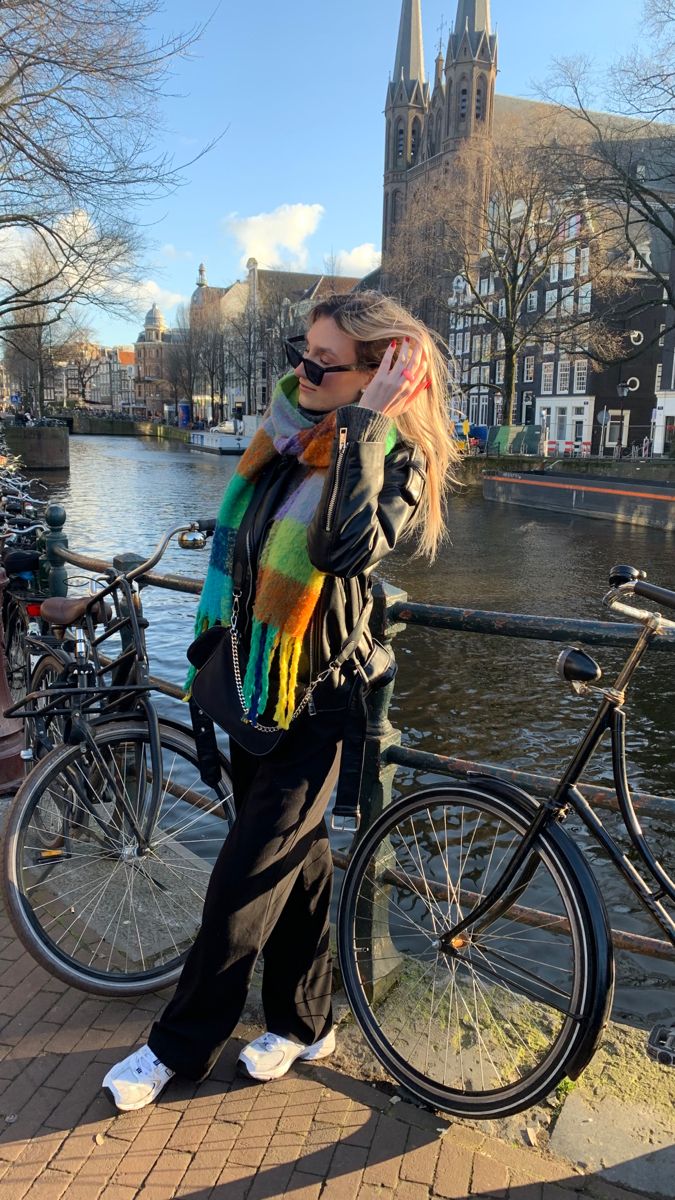 a woman standing next to a bike on the side of a river while talking on a cell phone