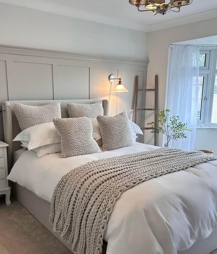 a bed with white linens and pillows in a bedroom next to a large window