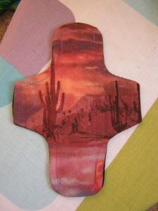 a piece of art that looks like a cross on the ground with cactus trees in the background