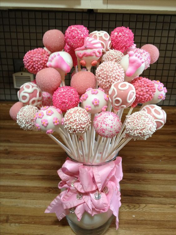 a vase filled with lots of pink and white cake pops on top of a wooden table