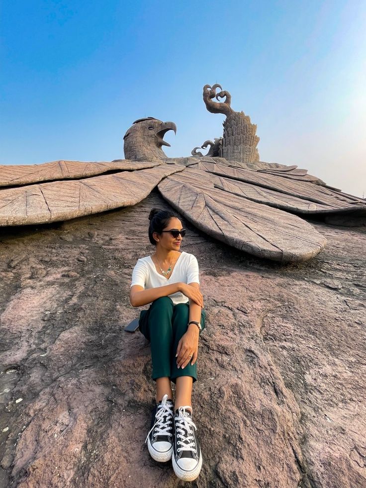 a woman sitting on top of a large rock next to an eagle shaped structure in the sky