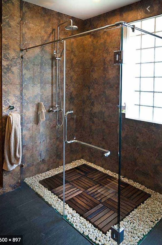 a walk in shower sitting next to a window on top of a wooden floor covered in pebbles