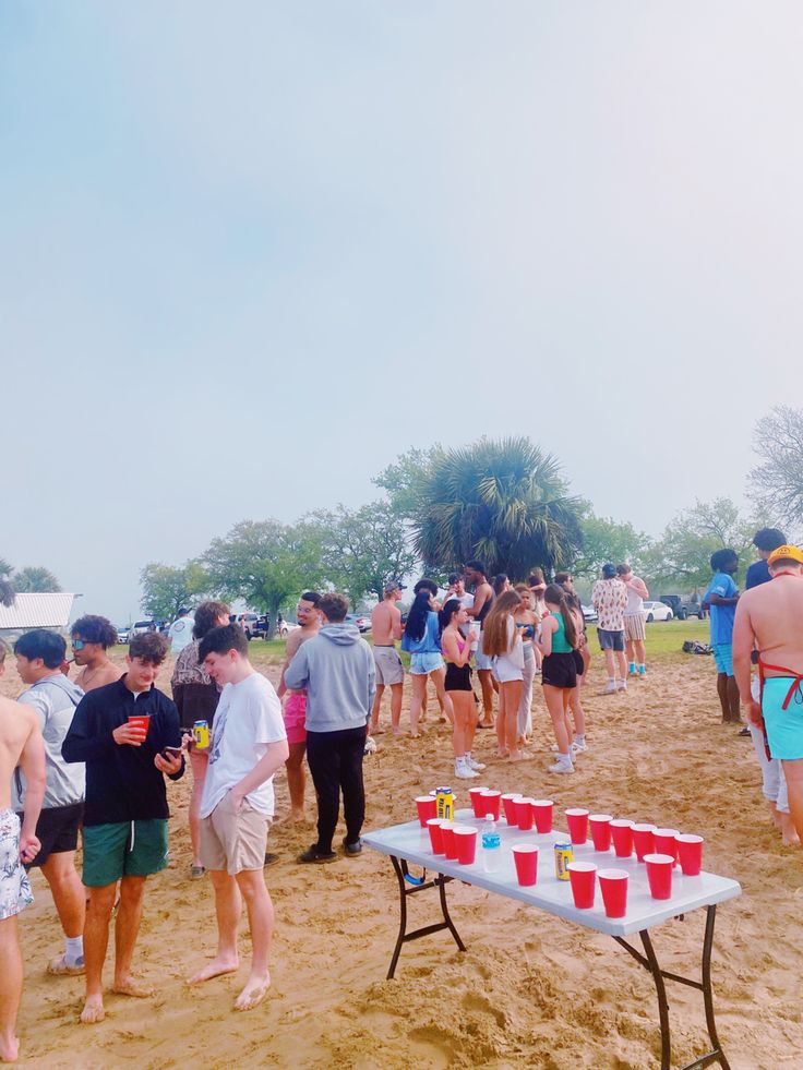 a group of people standing on top of a sandy beach next to a picnic table