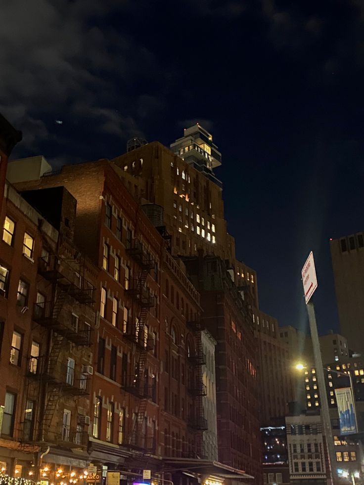 a city street at night with tall buildings and traffic lights on the side of it