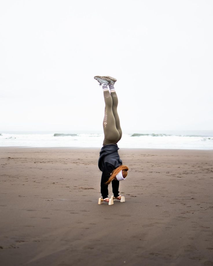 a person doing a handstand on the beach with their feet in the air