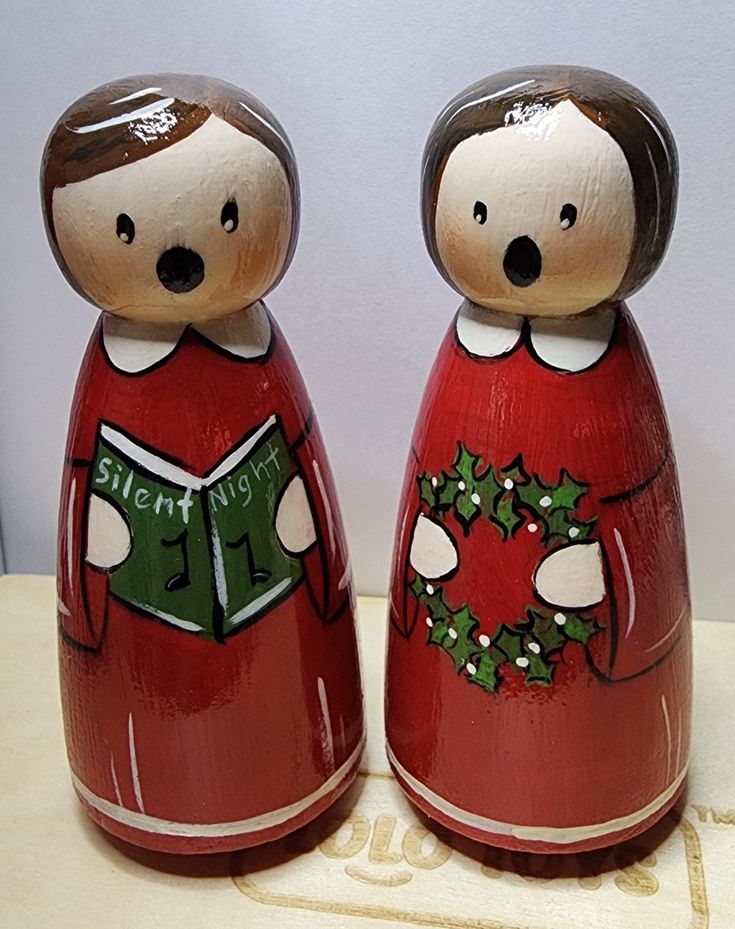 two wooden figurines with christmas decorations on them sitting next to each other in front of a white wall