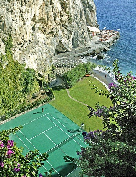 an aerial view of a tennis court in the mountains overlooking the ocean and cliffs with people playing on it