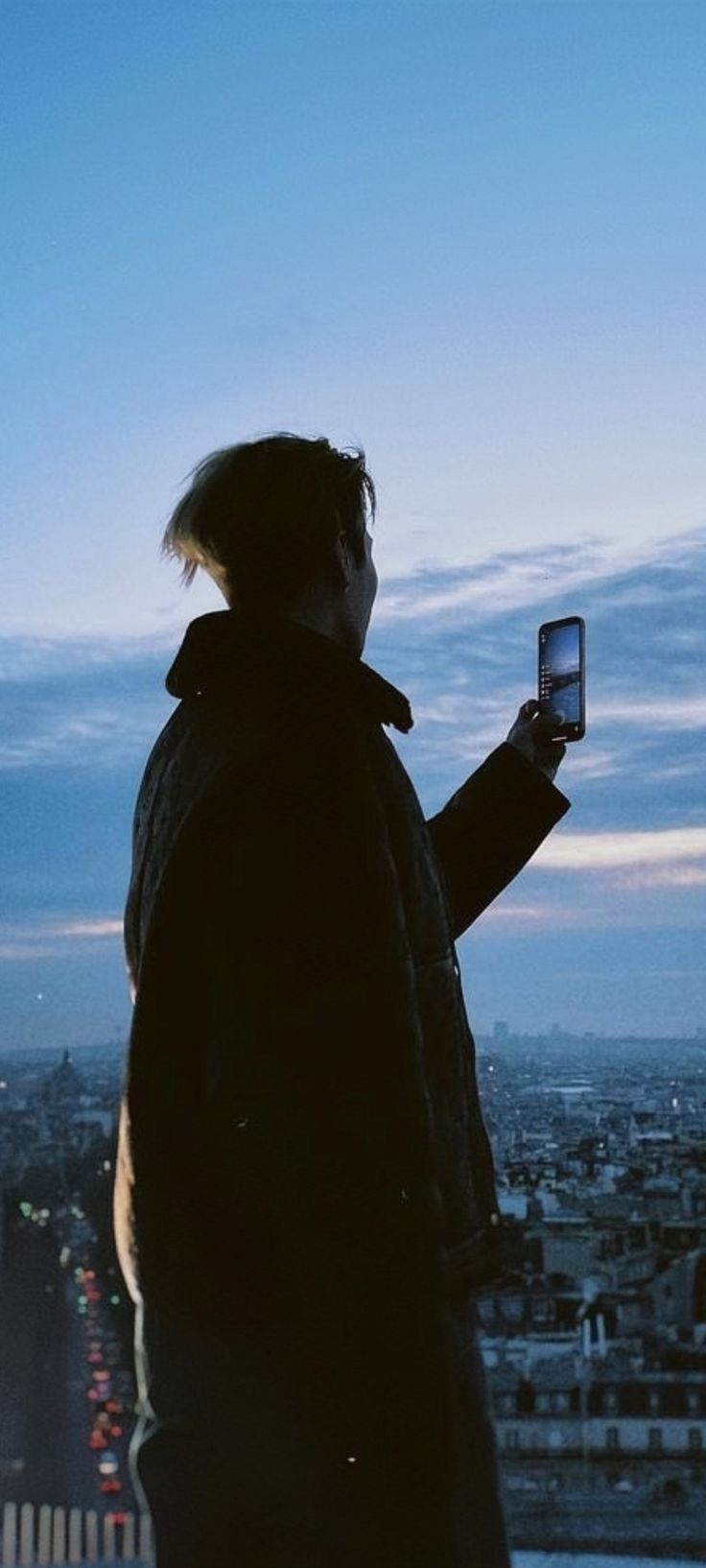 a man standing on top of a tall building holding a cell phone in his hand