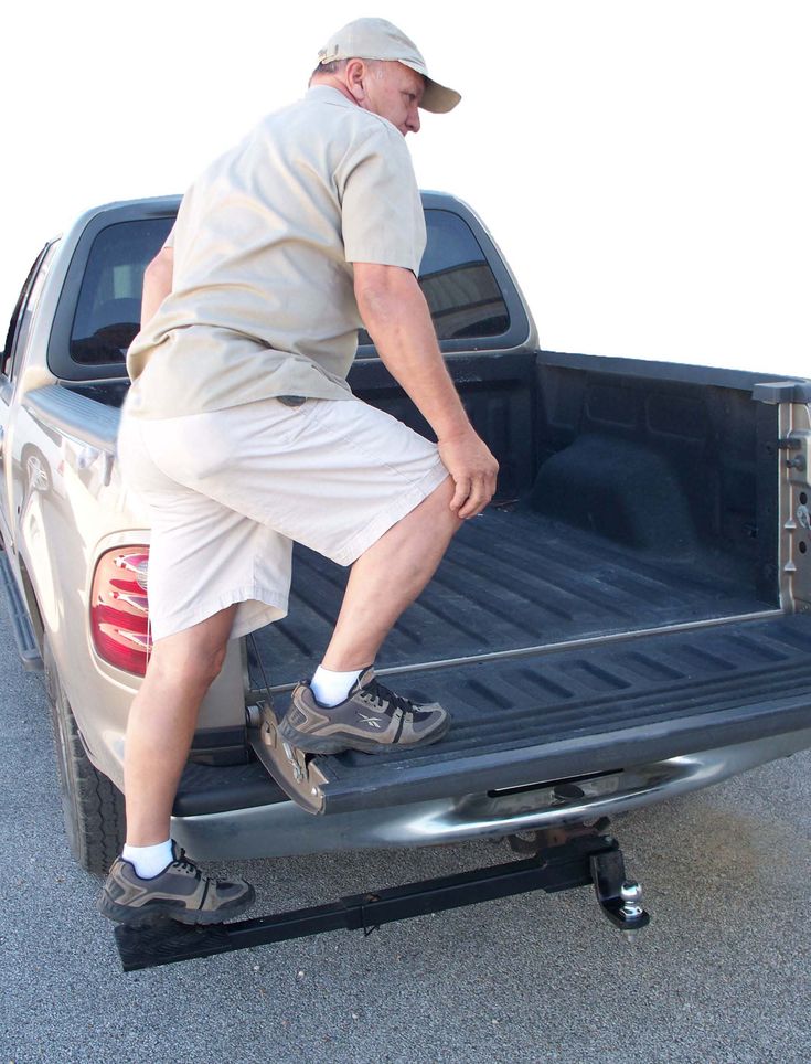 a man in shorts and a hat standing on the back of a pickup truck bed