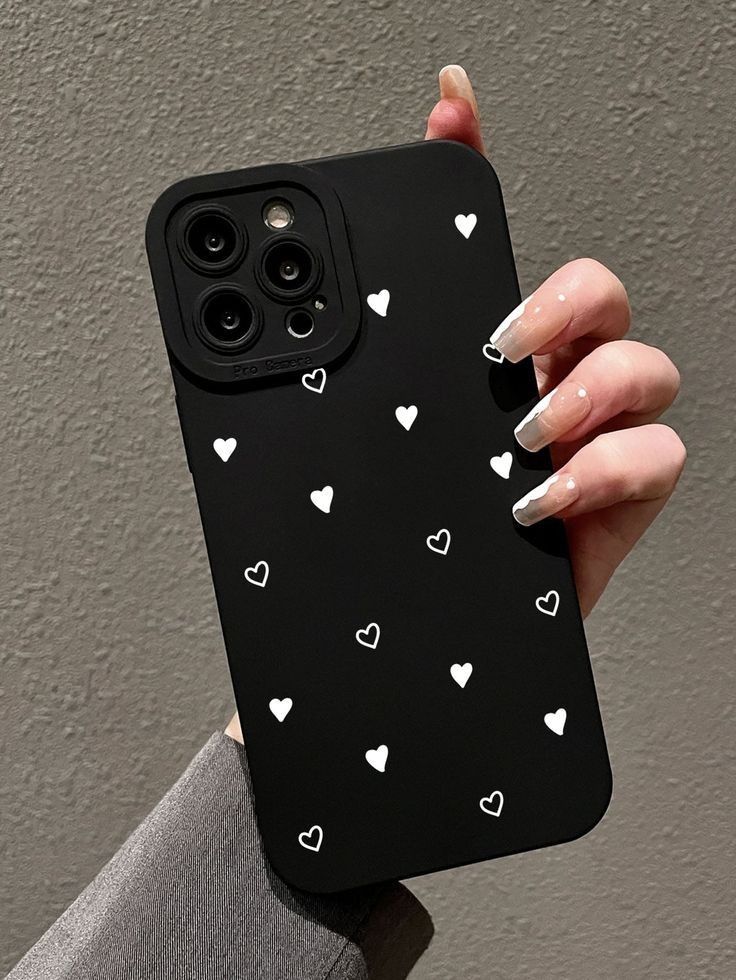 a woman's hand holding a black phone case with white hearts on the back