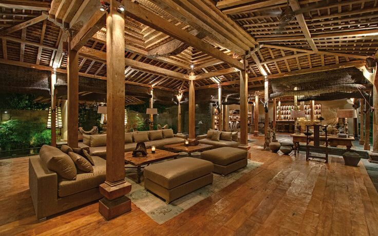 a living room filled with lots of furniture under a wooden roof covered in bamboo beams