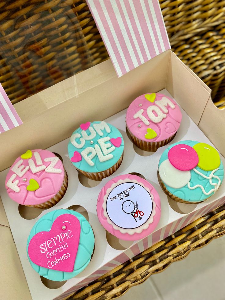 some cupcakes are in a box on a wicker table with pink and blue frosting