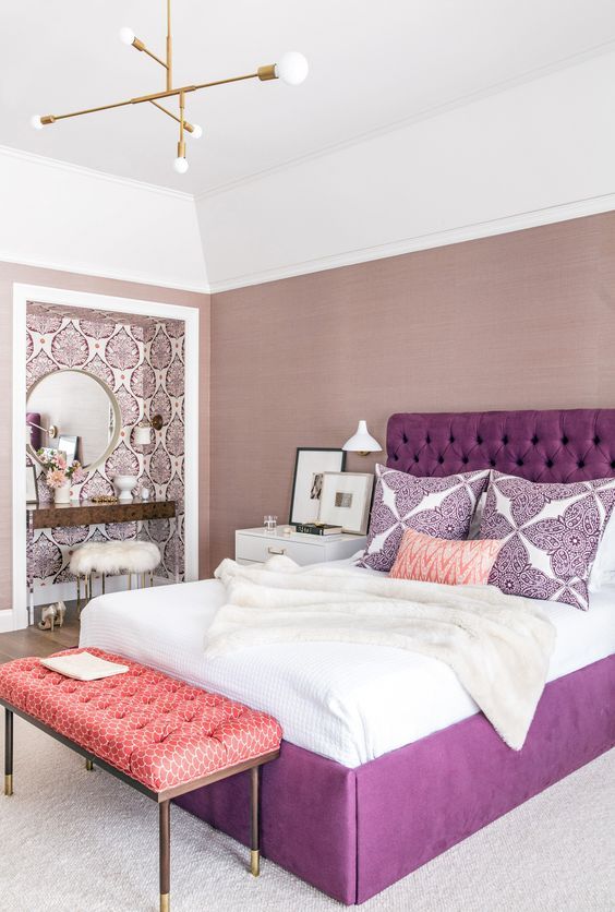 a bedroom with a large bed, purple and white pillows, pink accents and a mirror on the wall