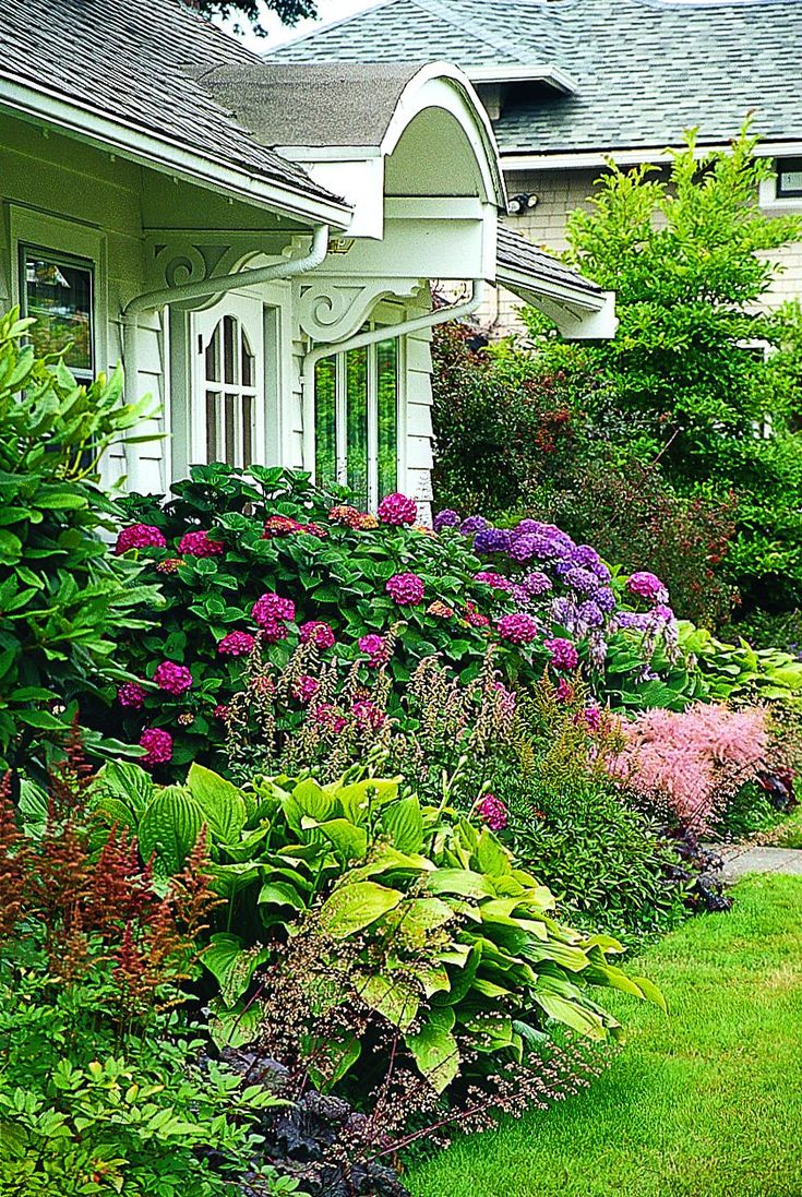 the house is white and has many flowers in front of it, along with green grass