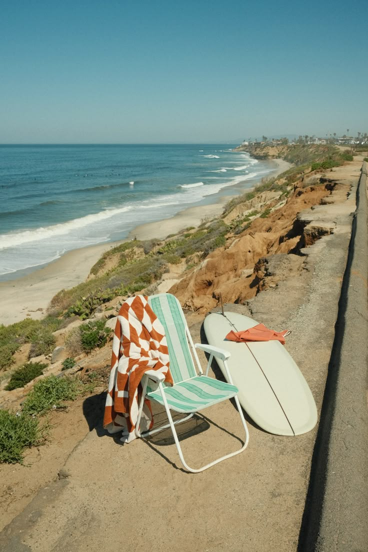 two surfboards and a chair on the side of the road next to the beach