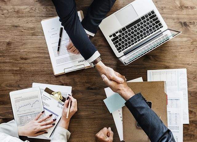 two people shaking hands over papers and laptops on a wooden table with the caption kingwood bank