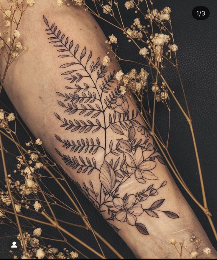 a black and white photo of a flower tattoo on the left arm, with flowers in the background