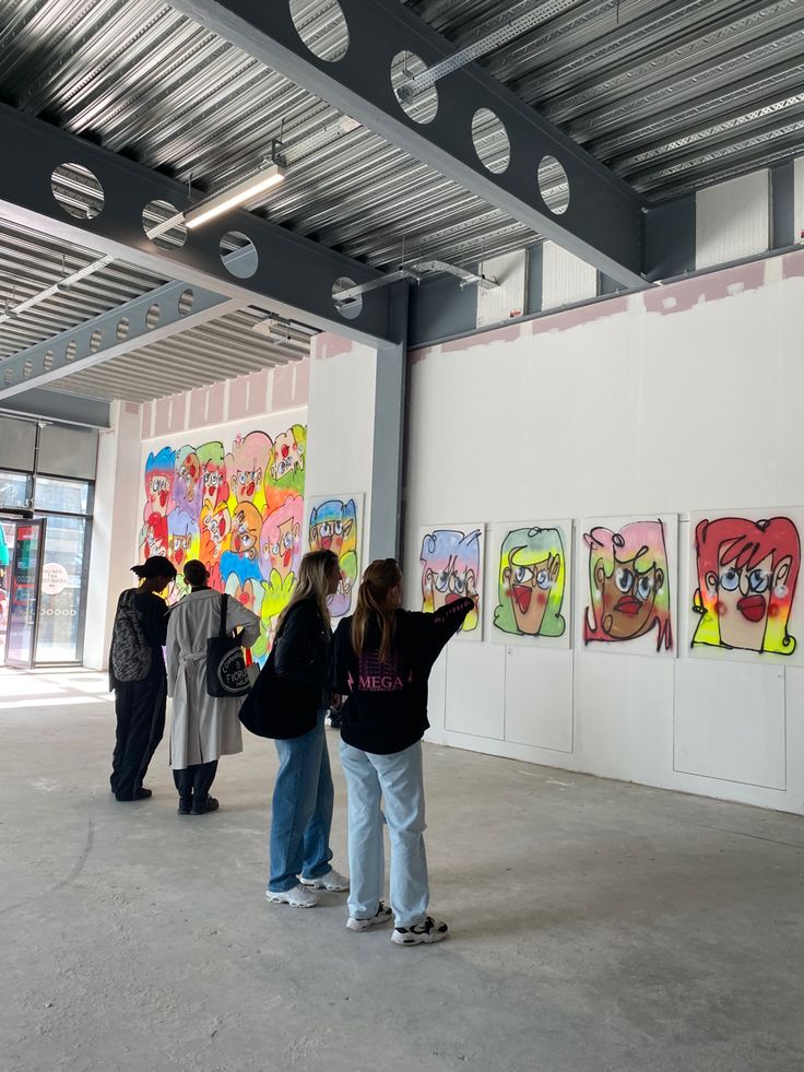 several people are looking at cartoon paintings on the wall in an empty room with white walls