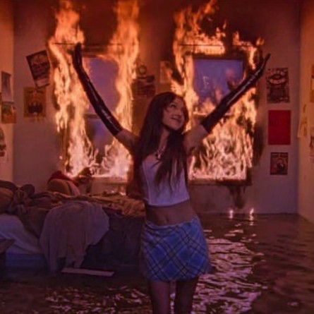 a woman standing in a flooded room with her arms out and fire coming from the ceiling