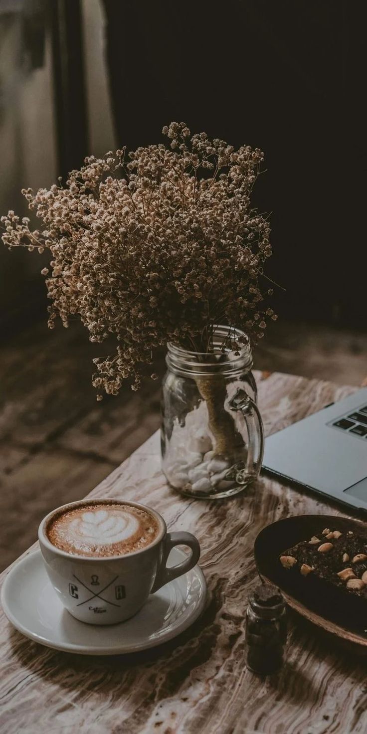 a cup of coffee sitting on top of a wooden table next to a laptop computer