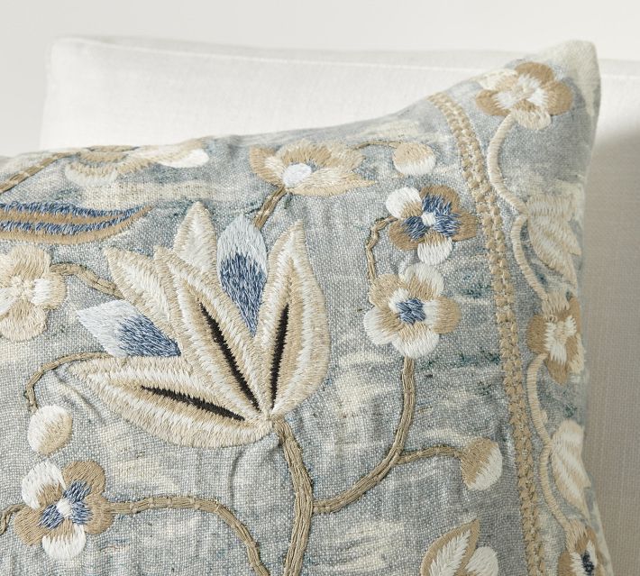 a close up of a decorative pillow on a white couch with blue and gold flowers