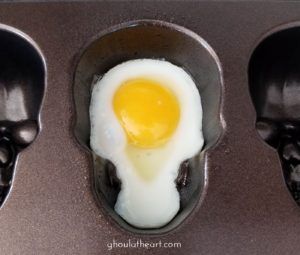 three black spoons with an egg in the middle and two skull heads on each side