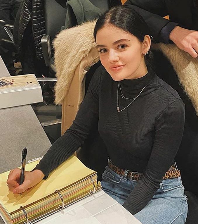 a woman sitting at a desk writing on a piece of paper with a pen in her hand