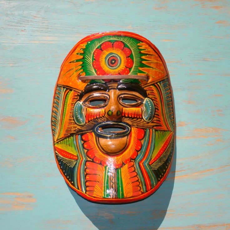 a colorful mask is hanging on a blue wooden wall with a green and orange background