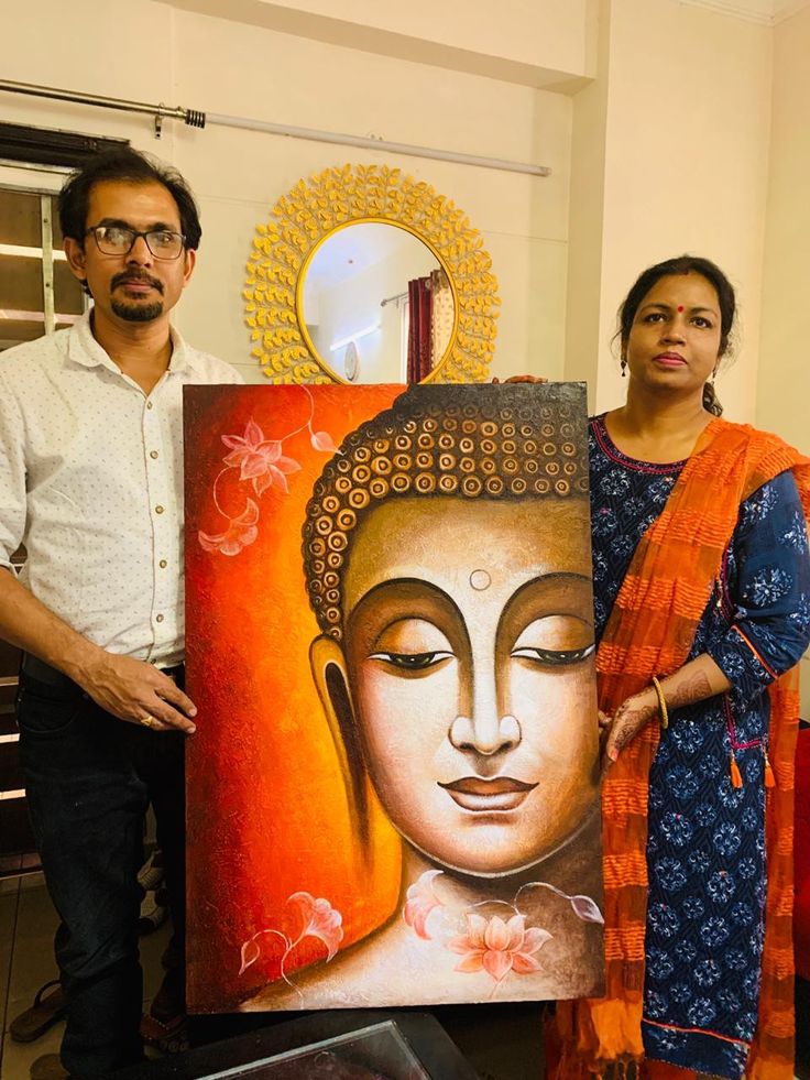 two people standing in front of a painting with an image of buddha on it and another person holding up a piece of art