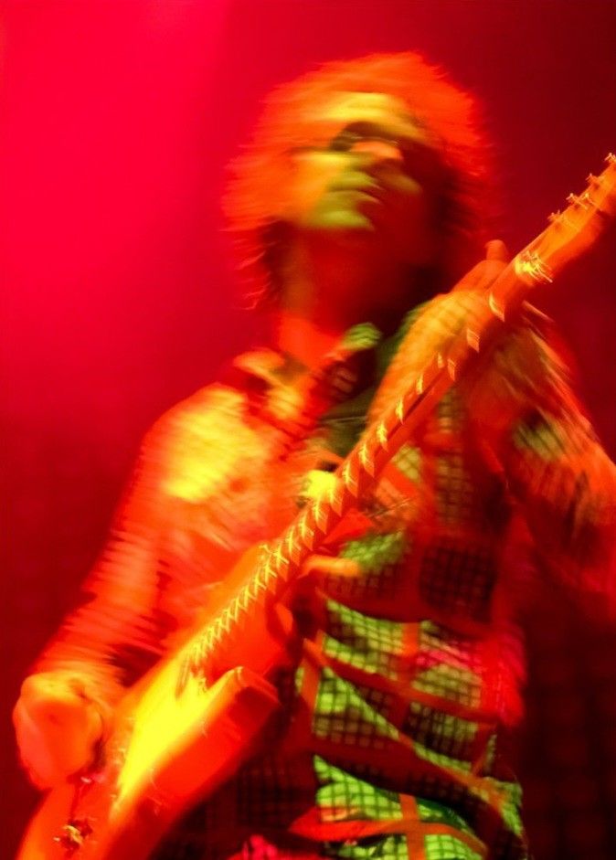 a man playing an electric guitar in front of a red light with his hair blowing