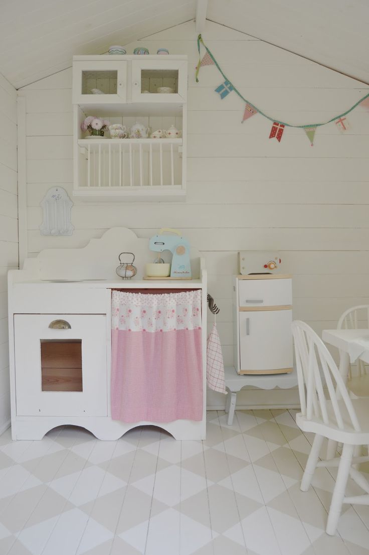 a white and pink play kitchen with lots of toys on the table in front of it