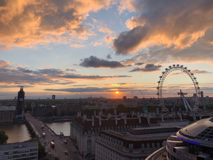 the sun is setting over an urban area with tall buildings and a ferris wheel in the distance