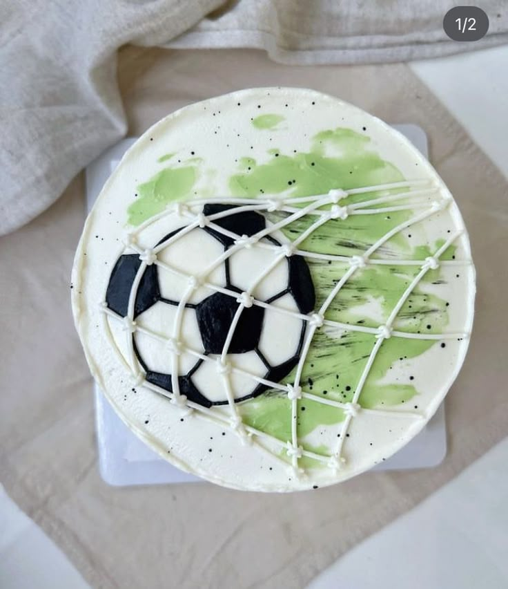 a soccer ball on top of a white cake with green splatters and icing