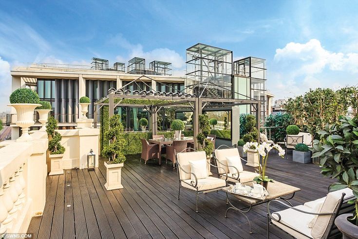 an outdoor deck with chairs, tables and potted plants on the top floor in front of a large building