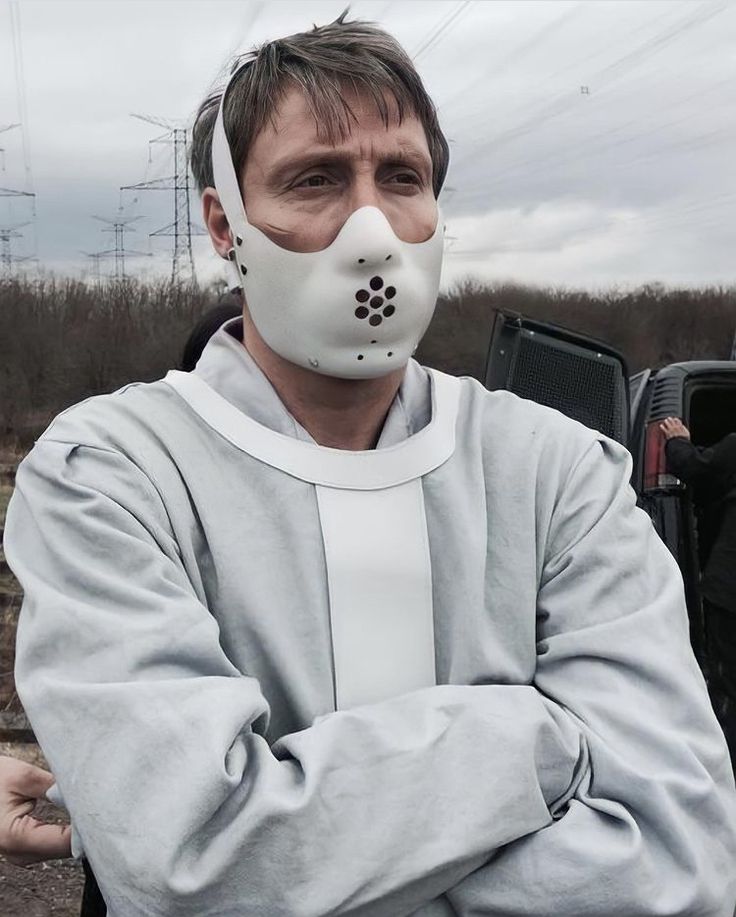 a man wearing a gas mask with his arms crossed, standing in front of a truck